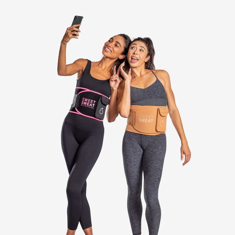 Two women wearing Sweet Sweat® waist trimmers with Sweet Sweat® phone cases attached to them.