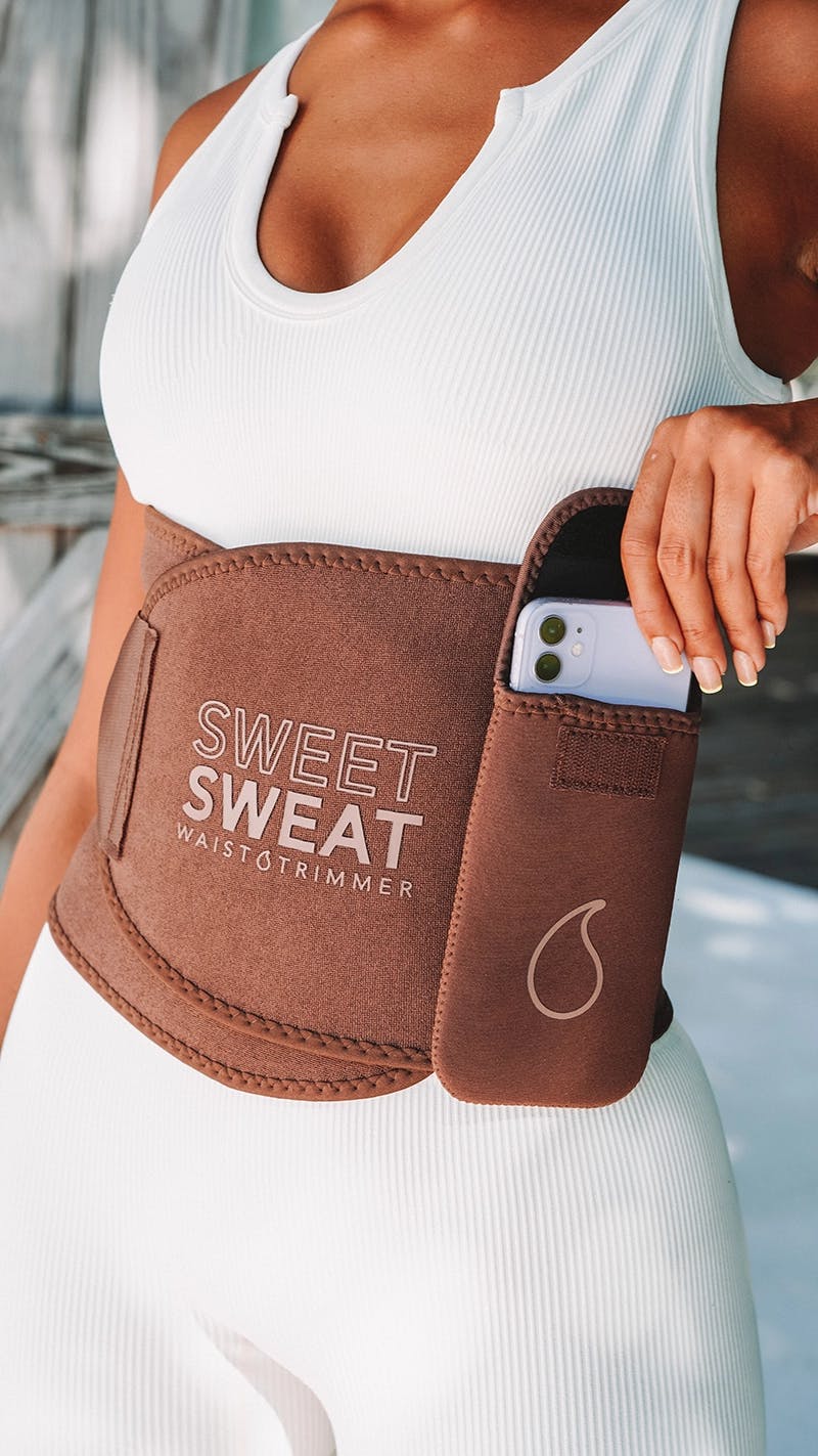 Two women wearing Sweet Sweat® waist trimmers with Sweet Sweat® phone cases attached to them.