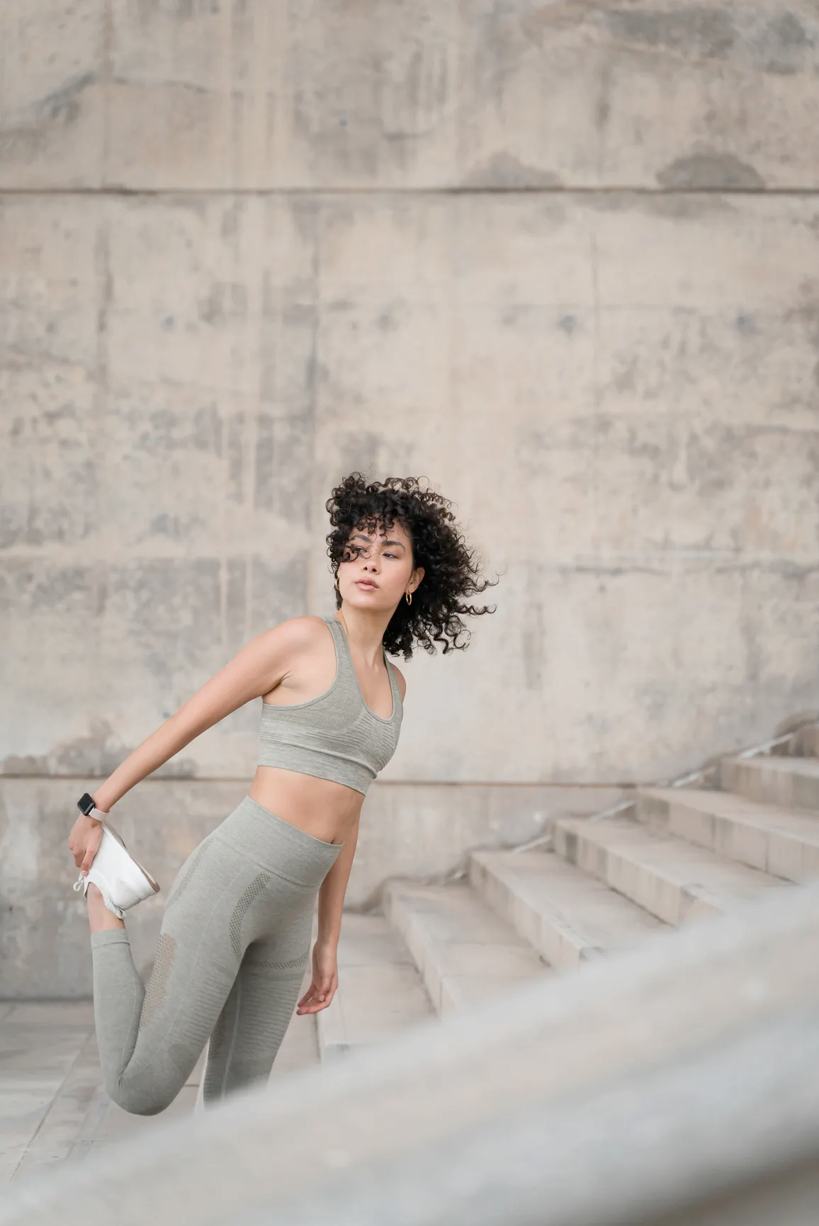 Woman in workout attire stretching her leg outside on a staircase.